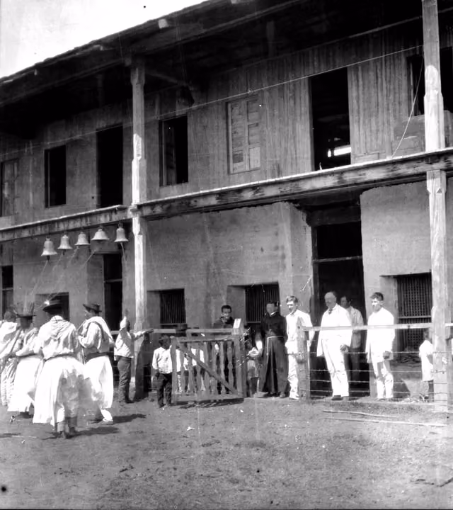 Indigenous people dancing outside the mission convent, with two Franciscan friars